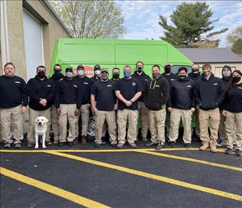 Group of men & women standing in uniforms and masks in front of Servpro trucks